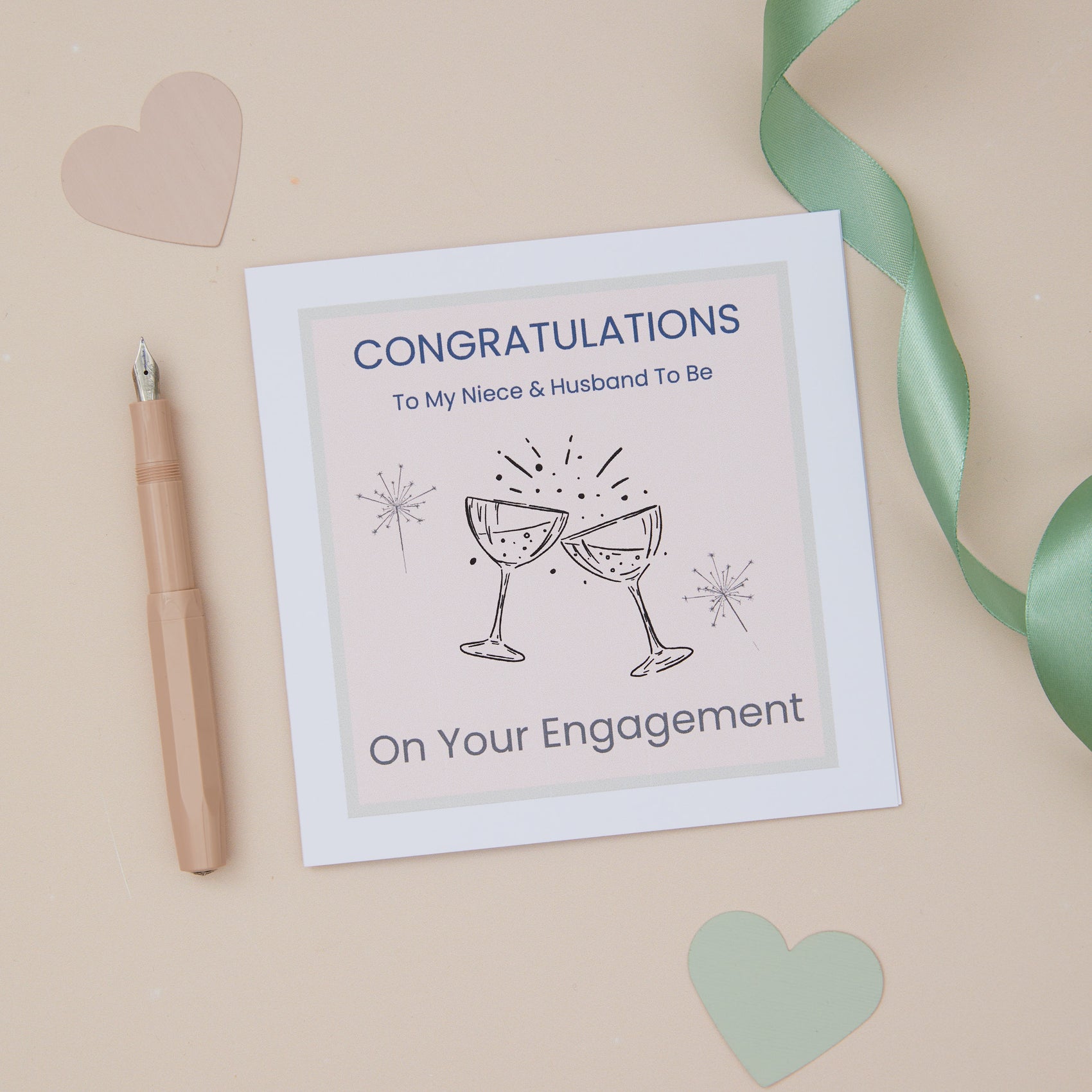 A Niece colourful engagement congratulations card with two glasses toasting, placed on a neutral background with a pen and decorative hearts.