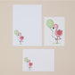Pink Flamingos Writing Set Illustrations. Three illustrations of pink flamingos with green balloons on a beige background. One shows the writing paper, another shows the postcard, and another the front of the envelope all featuring the pink flamingos and green balloons