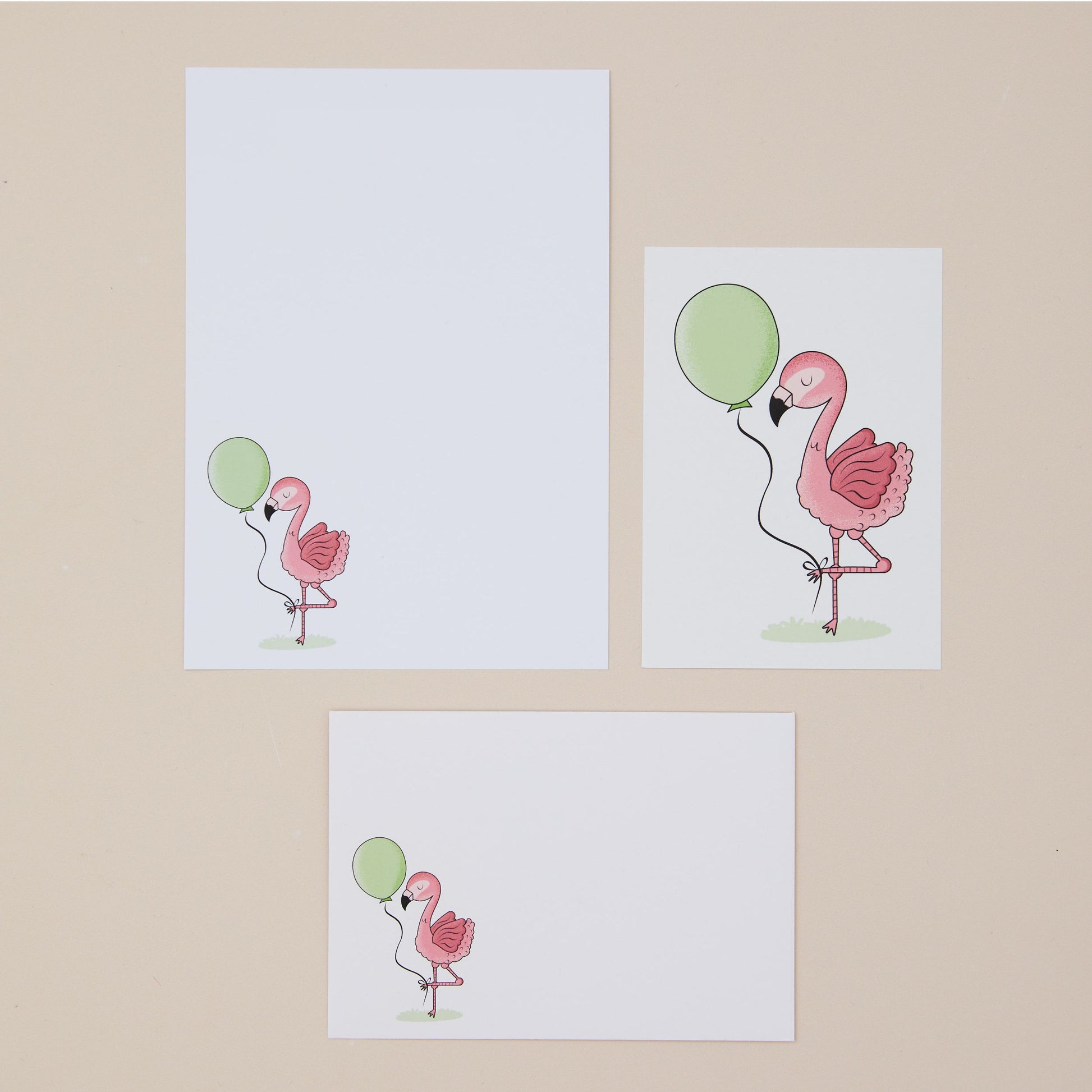 Pink Flamingos Writing Set Illustrations. Three illustrations of pink flamingos with green balloons on a beige background. One shows the writing paper, another shows the postcard, and another the front of the envelope all featuring the pink flamingos and green balloons
