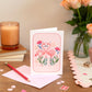 Pinks Flamingos Card Set of 8 with pink  envelopes, placed on a table with a candle and floral arrangement in the background.