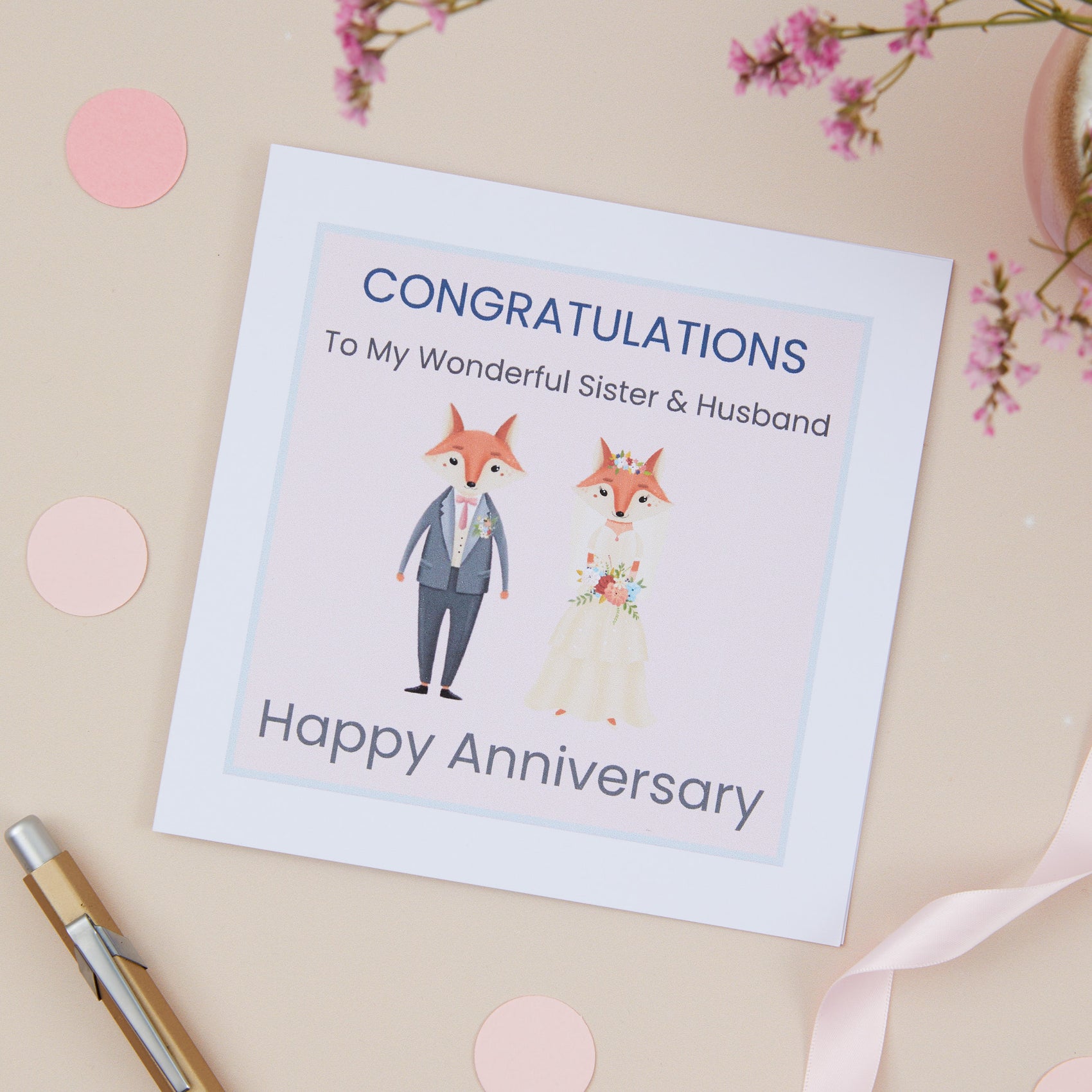 Sister & Brother In Law  greeting card with an illustration of a fox couple dressed in bridal attire, with a 'Congratulations Happy Anniversary' message, placed on a flat surface with decorative elements around it.
