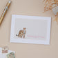 A Sympathy card with an illustration of a cheetah and its cub, with the text 'Thinking Of You' on the front. The card is placed on a beige background with a pen and some decorative elements.