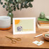 A thank you note card with a graphic of an elephant and a sun illustration, placed on a wooden table with a cup, scissors, and other stationery items in the background.