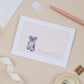 A thank you card with a koala design, placed on a desk with a pen, ribbon, and decorative elements.