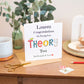 Theory Test Greeting card congratulating on passing theory test, The word theory is spelt out in a patch work type font. The card is placed on a wooden surface with a mug and stationery items.