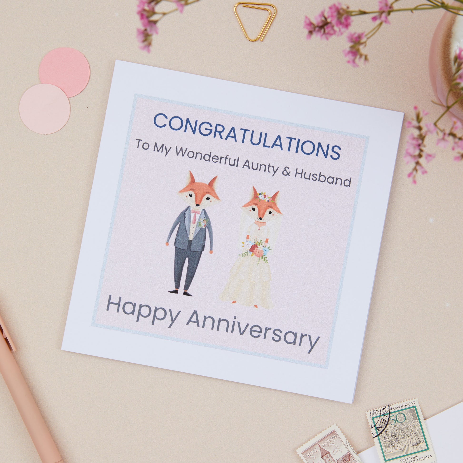 A Aunty & Uncle wedding anniversary card with a cute Mr & Mrs Fox illustration, with congratulatory text, placed on a neutral background with some decorative elements.
