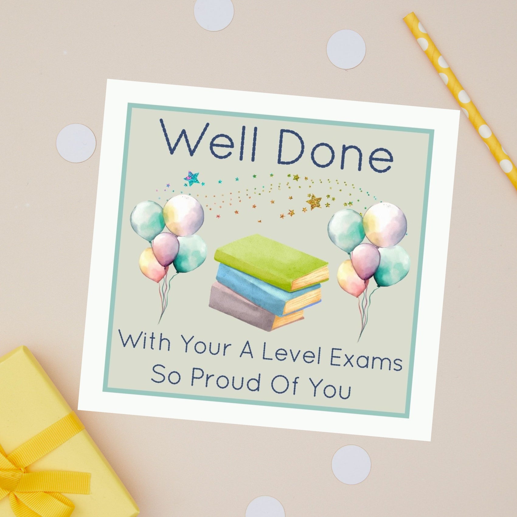 Well Done A Level Exams Card Greeting card with 'Well Done with your A Level exams so proud of you' message. It also has balloons of different colours and a stack of books in between them. The card sits on a beige background with stationery items and presents 