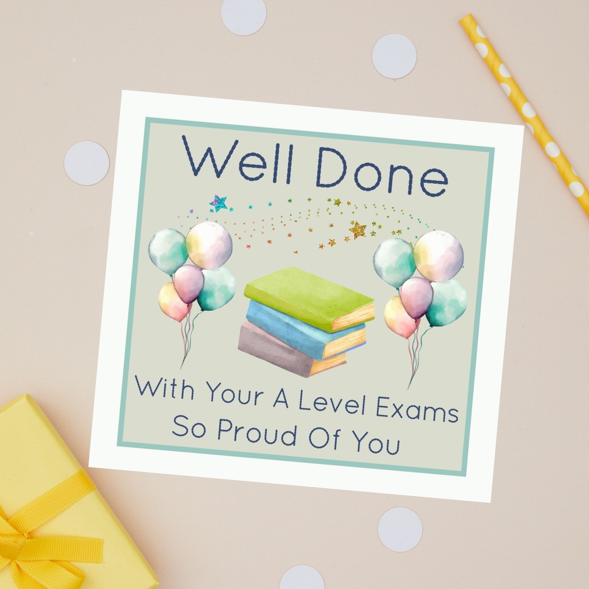 Well Done A Level Exams Card Greeting card with 'Well Done with your A Level exams so proud of you' message. It also has balloons of different colours and a stack of books in between them. The card sits on a beige background with stationery items and presents 