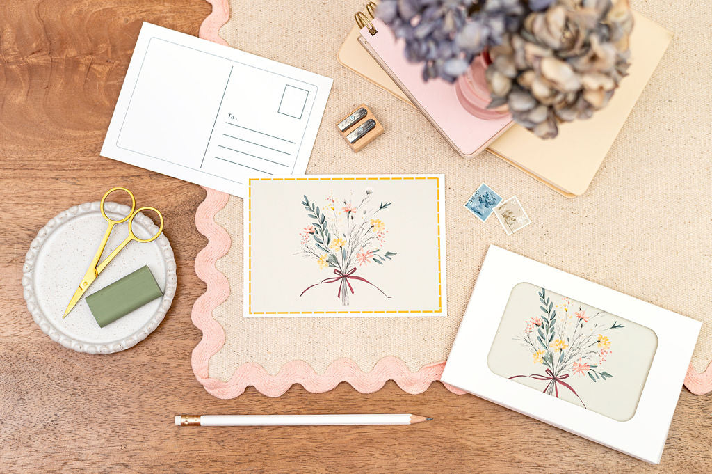 A6 Postcard with a Bouquet, with a Yellow Border. The Card is on a desk, surrounded by Stationery.