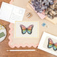 A6 Postcard with a Butterfly, with a yellow Border. The Card is on a desk, surrounded by Stationery.