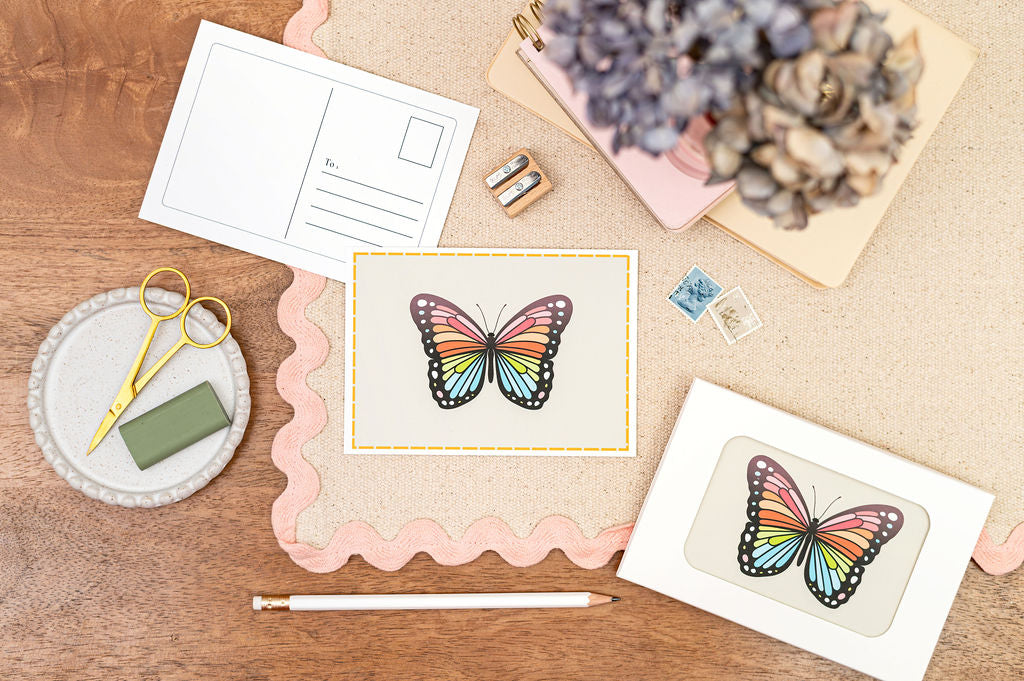 A6 Postcard with a Butterfly, with a yellow Border. The Card is on a desk, surrounded by Stationery.