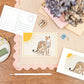 A6 Postcard with a Cheetah and it's Baby, with a yellow sun in the background. The Card is on a desk, surrounded by Stationery.