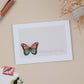 A sympathy greeting card with a colourful butterfly design on the front, with the text 'Thinking Of You' displayed, placed on a neutral background with a white envelope beside it.