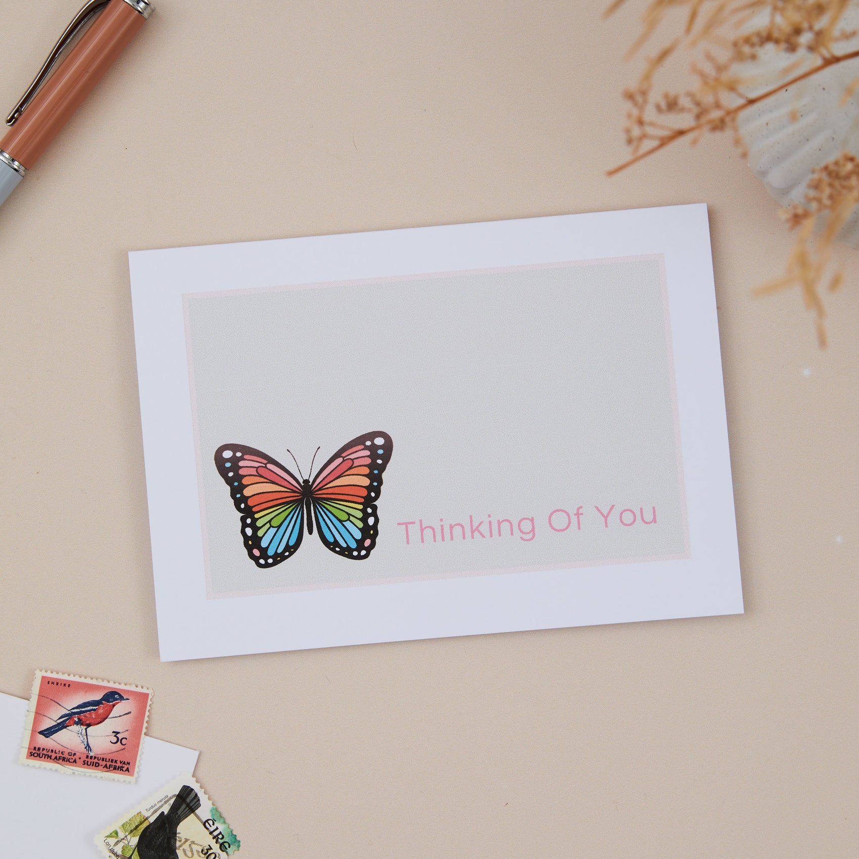 A sympathy greeting card with a colourful butterfly design on the front, with the text 'Thinking Of You' displayed, placed on a neutral background with a white envelope beside it.